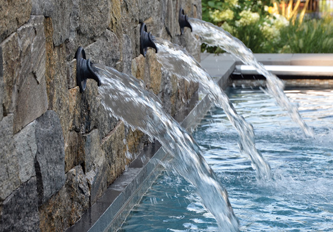 Natural stone veneer wall with water feature near a pool