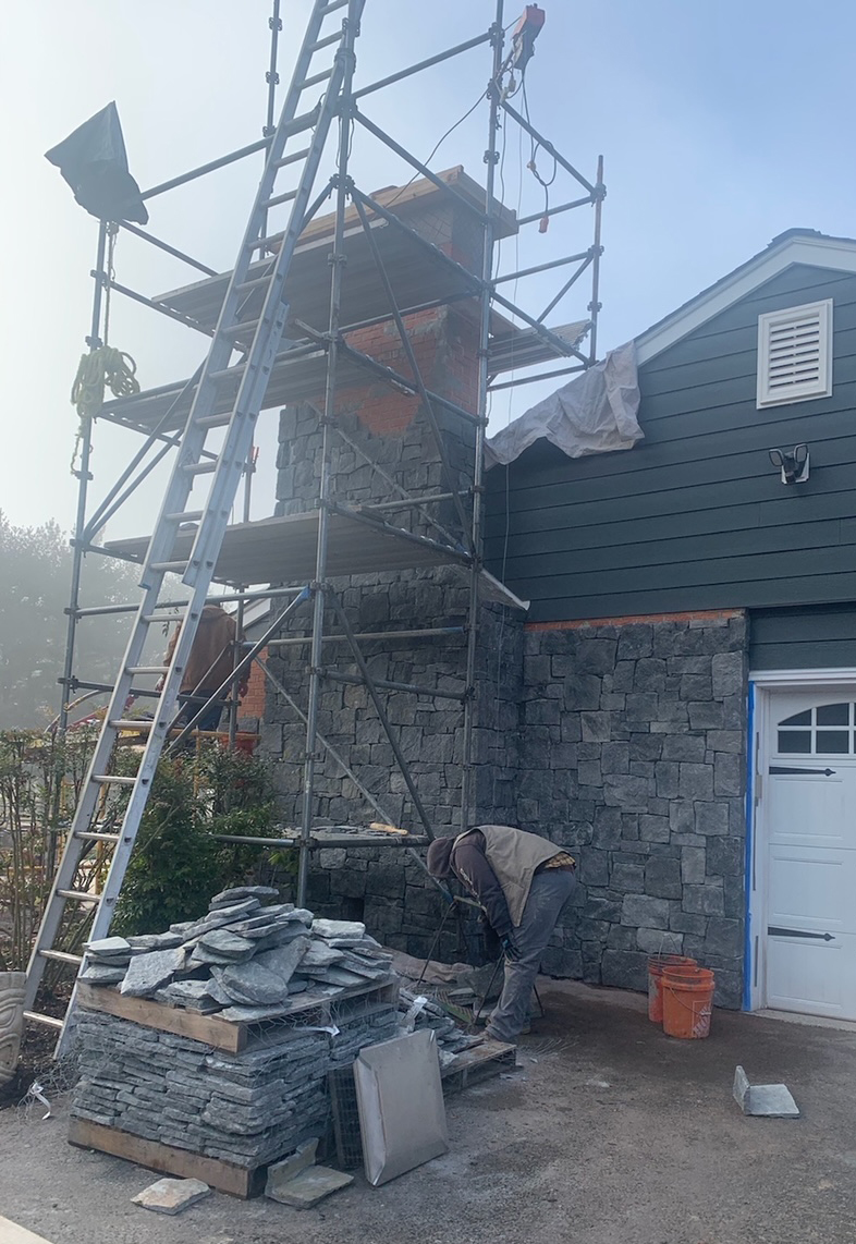 Masons installing stone veneer on a brick chimney